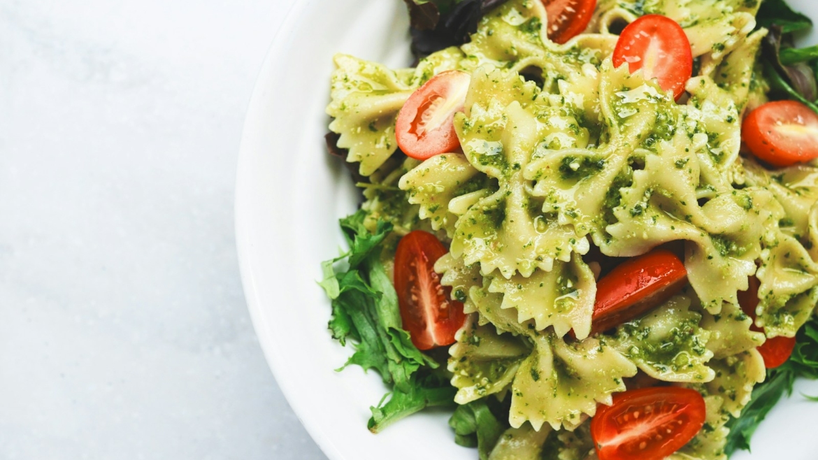 Pesto pasta with sliced tomatoes served on white ceramic plate